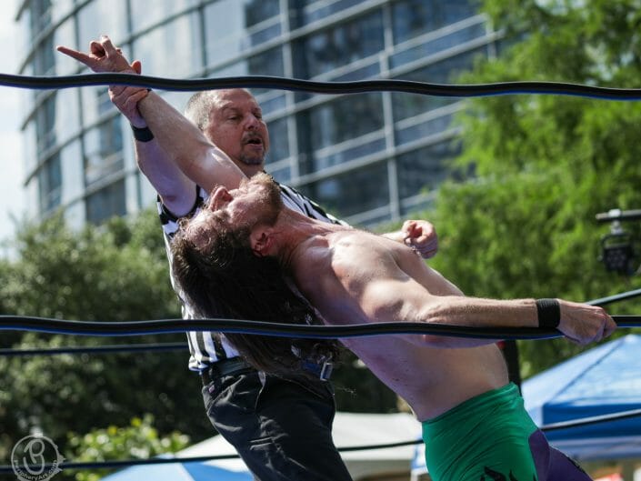 Referee holds up champion's hand in a wrestling match.